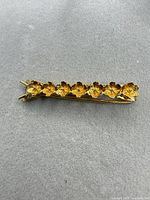 Full view of gold tone floral barrette on gray background