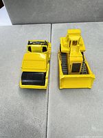 Front and rear view of both yellow die-cast vehicles on grey surface