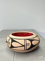 Side view of pottery bowl showing tan clay body, black geometric design, and red wax interior