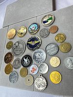 Overall view showing 26 challenge coins and tokens on grey board