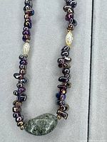 Close-up of purple iridescent bead necklace showing green stone pendant, iridescent beads and gold-tone/pearl accent beads
