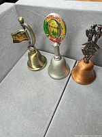 Three metal handbells in brass, silver, copper finishes