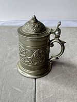Full view of miniature metal beer stein showing ornate relief and hinged lid