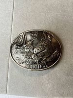 Front of belt buckle showing hog motif and slogan
