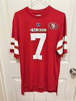 Front view of red 49ers jersey on hanger showing number 7 and sleeve stripes