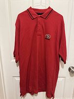 Full front view of red polo shirt on hanger showing overall condition and team logo