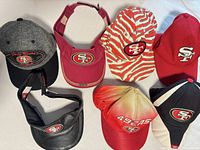 Seven SF 49ers hats and visors laid out for overview
