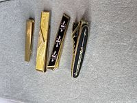 Front view of all four tie clips showing designs and enamel