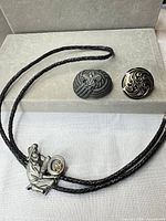 Full view of bolo tie with prospector slide and two conchos on grey background