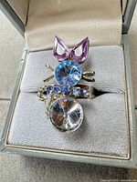Front view showing cat motif ring with clear body, blue head, lavender ears, collar stones, whiskers, tail