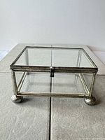 Front angled view of clear glass jewelry box with silver-tone metal frame and feet