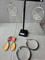 All three earring pairs displayed: chain fringe dangles hanging, orange stone drops, silver hoops