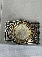 Front view of belt buckle showing coin and two-tone scroll design