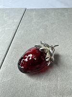 Full view of cranberry red strawberry-shaped glass vial with leaf cap