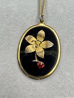 Front view of oval pendant showing gold flower, black enamel, red stone