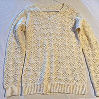 Full front view of cream pointelle V-neck sweater on hanger