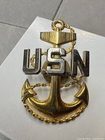 Front view of gold-tone anchor with silver-tone USN letters, screw-back visible