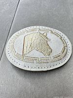 Front view of oval leather belt buckle showing horse embroidery and overall wear