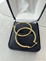 Two gold-tone hoop earrings in black jewellery box