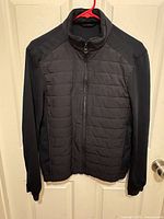 Full front view of black quilted jacket on hanger