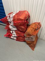 Four stacked red/orange mesh bags plus one leaning bag showing contents