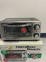 Toaster oven atop its box, front view showing controls and branding