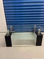 Front view showing glass top, chrome posts, black wood legs, frosted lower shelf