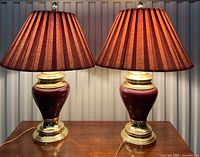 Front view of both matching burgundy ceramic and brass table lamps with pleated fabric shades