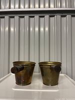 Front view of both brass saucepans showing wood handles and patina