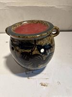 angled view of glazed ceramic jar candle showing side handles, cutout holes and red wax fill