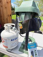 Trap unit with base, pole, adhesive ribbon visible beside propane tank (not included) and boxed refill