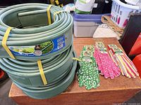 Stacked green lawn edging rolls and assorted gloves on table