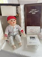 Doll in packaging with boxes, COA and baseball visible