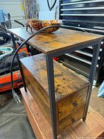 Oblique view of end table showing top surface, metal frame, drawers, power cord, bowl accessory