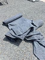 Two large gray felt mat pieces unrolled on gravel