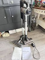 Vacuum on charging stand with two brush heads, charger, manuals visible