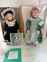 Both dolls side by side with certificates, stands and boxes visible
