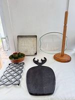 Overview showing sheet pan, glass dish, paper towel holder, ceramic olive dish with pots, cast iron trivet, carved board