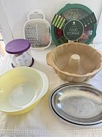 Group shot of Pyrex bowl, Pampered Chef bundt pan, two stainless trays, food storage container, grater, burger press