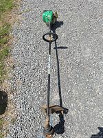 Full view of trimmer laid on gravel showcasing overall length, straight shaft and cutting head