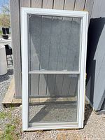 Full view of white vinyl single-hung window leaning against shed