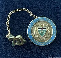 Front view of badge showing Ontario coat-of-arms, blue enamel ring text, attached 70 service bar on chain