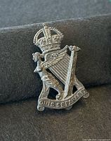Front view of Irish Regiment cap badge showing crowned harp, winged female figure and motto scroll
