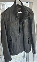 Front view of black leather jacket on hanger showing pockets and collar