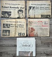 Five stacked newspapers displayed showing front pages and headlines