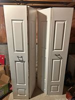 Four white raised-panel bi-fold door panels standing folded, pulls visible