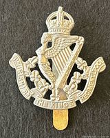Front view of cap badge showing crown, harp, winged figure, shamrocks, and scrolls