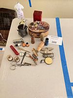 Full lot overview showing various sewing notions, heart-decorated box, mannequin figurine and metal container