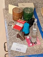 Lot overview showing tape pack, staplers, punch, candle holders, ChapStick, whistle, electronic device