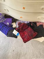 Drawer showing assorted sweaters including red patterned, black knit, purple garment